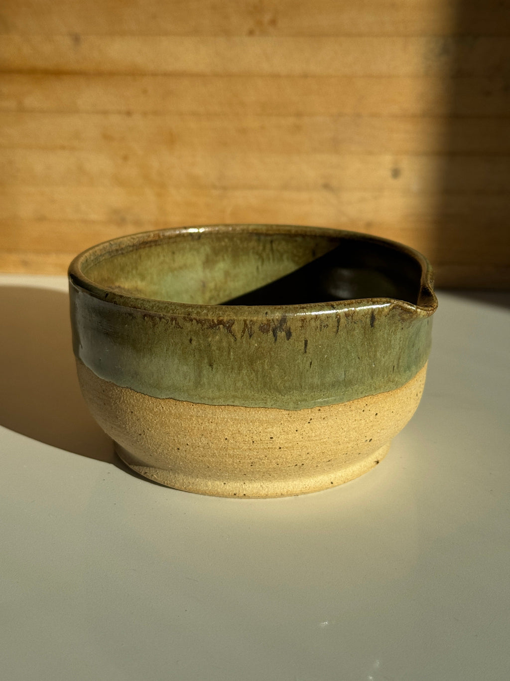 Ceramic bowl with green interior and beige exterior on a light clay surface