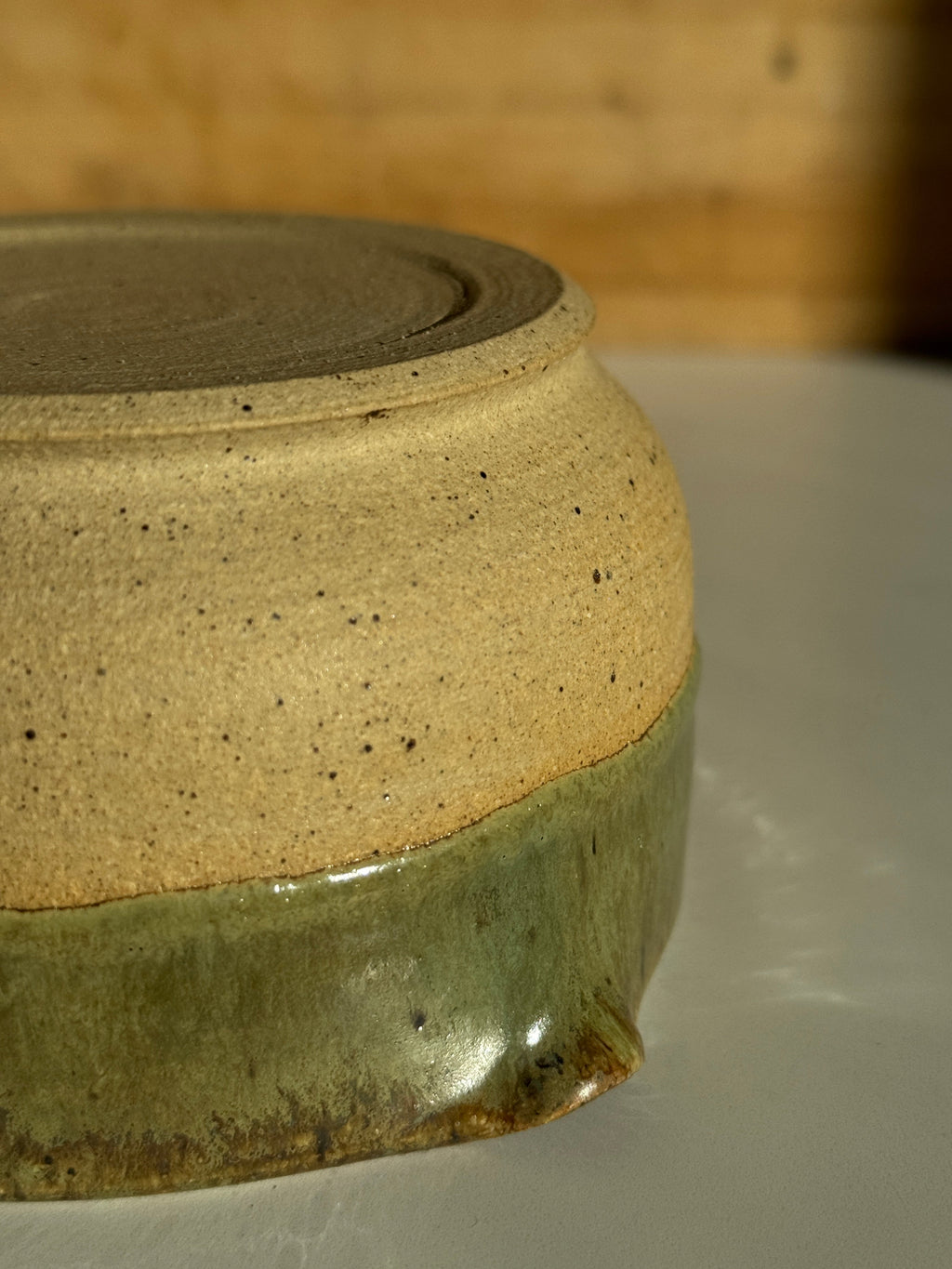 Ceramic bowl with green interior and beige exterior on a light clay surface bottom foot ring