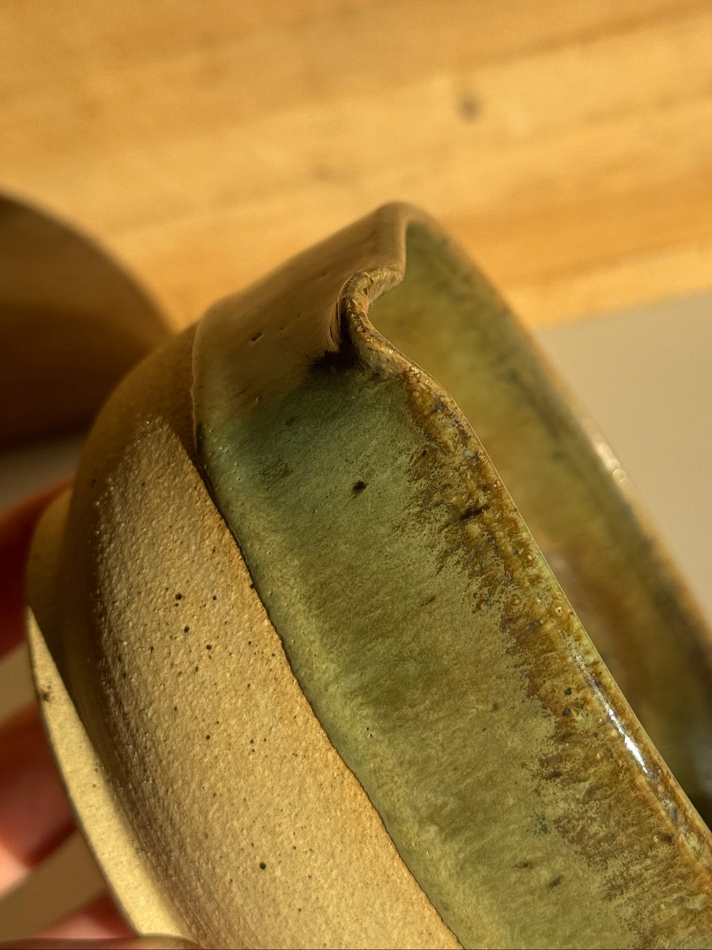 Ceramic bowl with green interior and beige exterior on a light clay surface spout