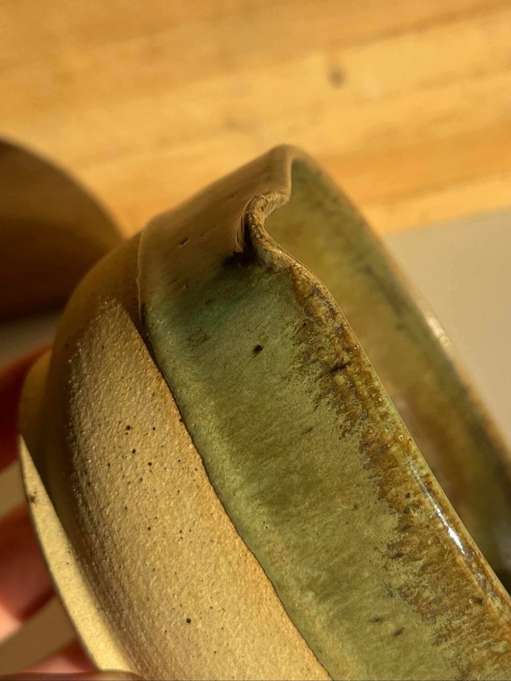 Ceramic bowl with green interior and beige exterior on a light clay surface spout
