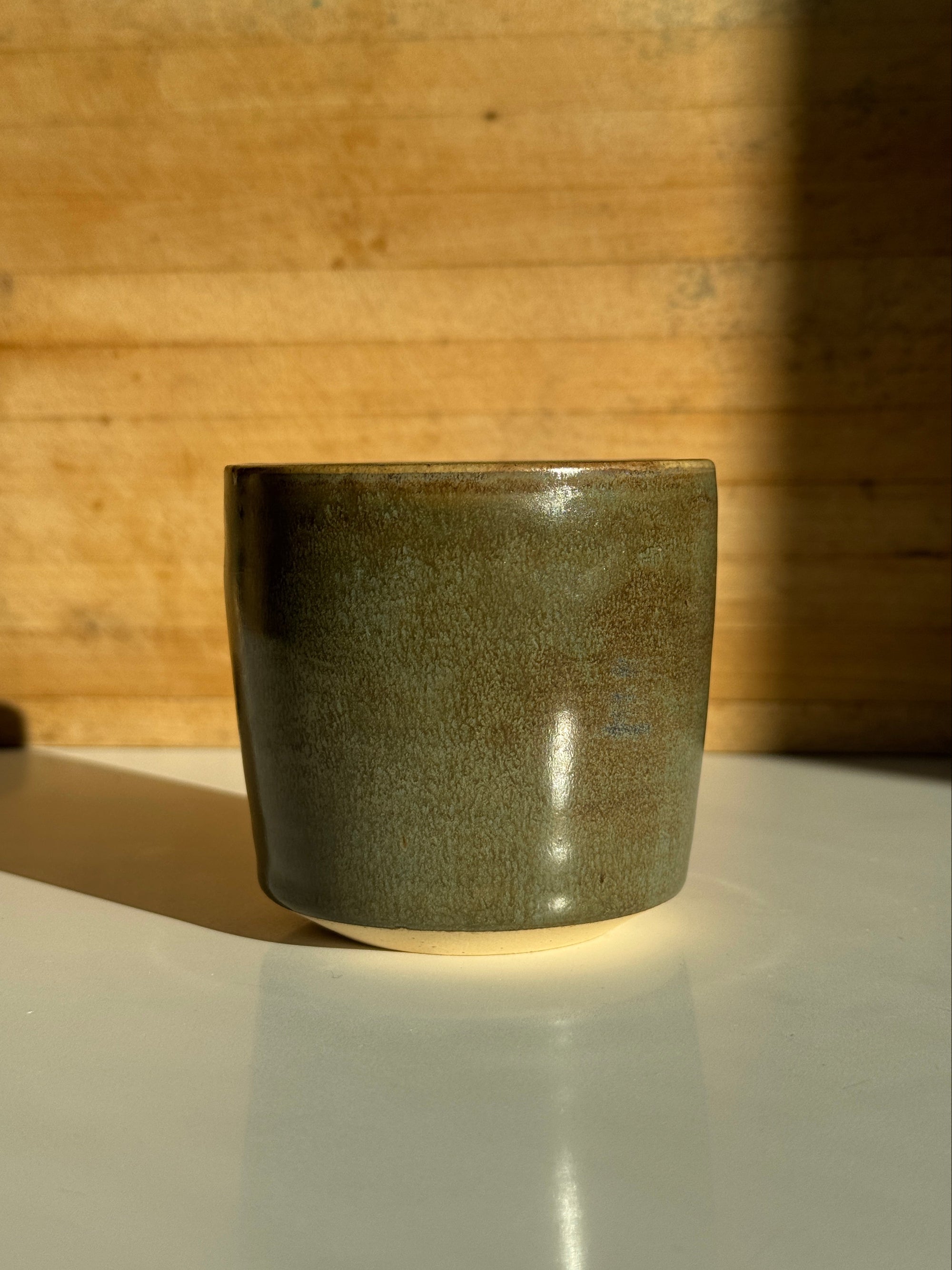 Olive green ceramic cup on light claybody