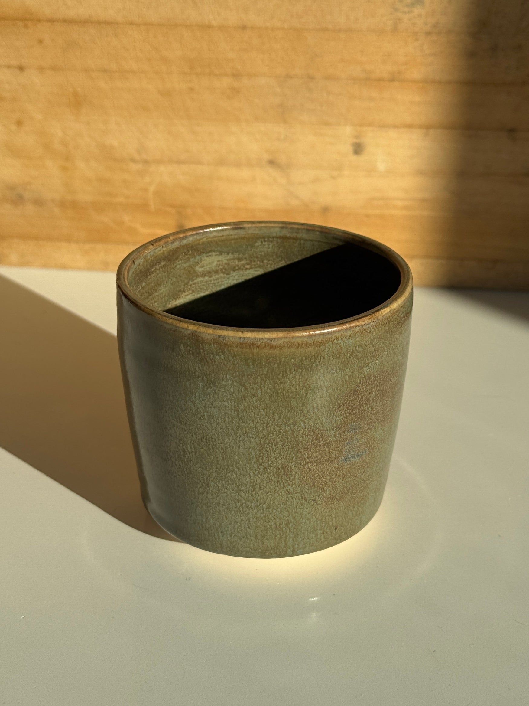 Olive green ceramic cup on light claybody